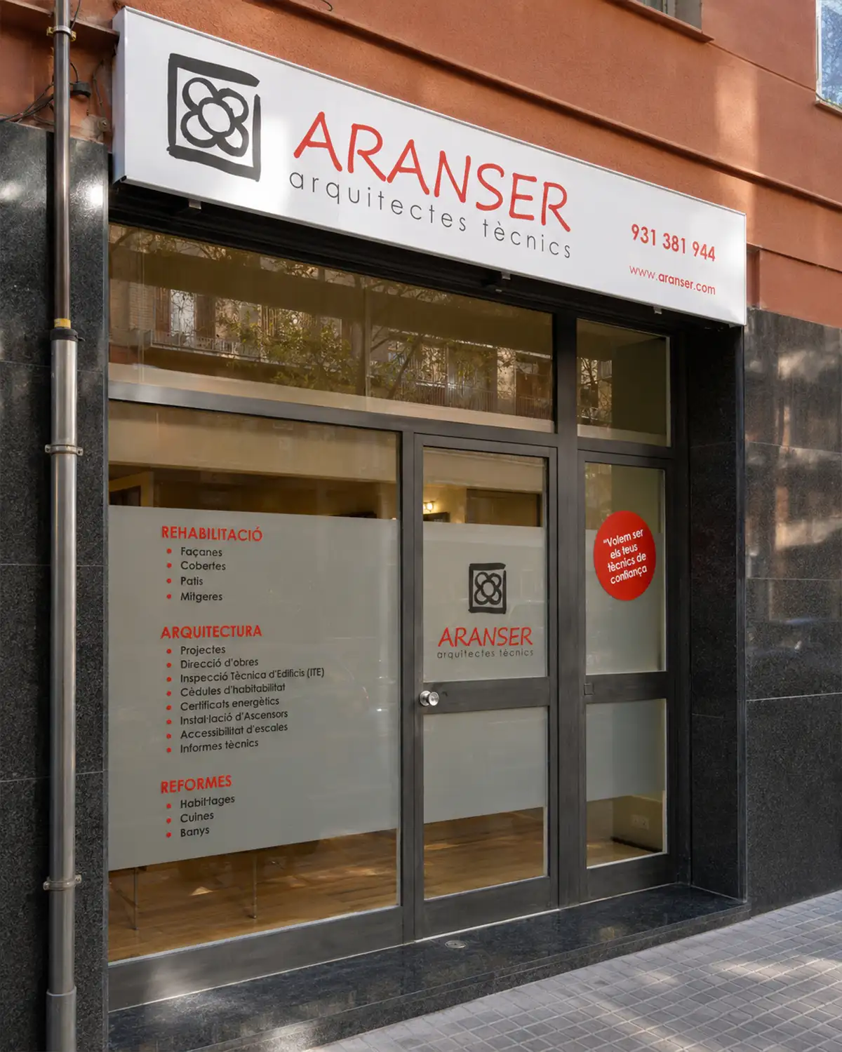 Rótulo superior y vinilos informativos aplicados en la fachada de un estudio de arquitectura técnica